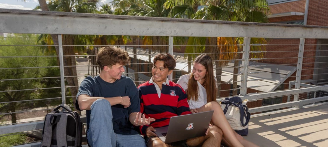 three students on campus sitting on bridge